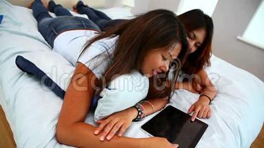 美丽快乐的姐妹们躺在床上用平板电脑